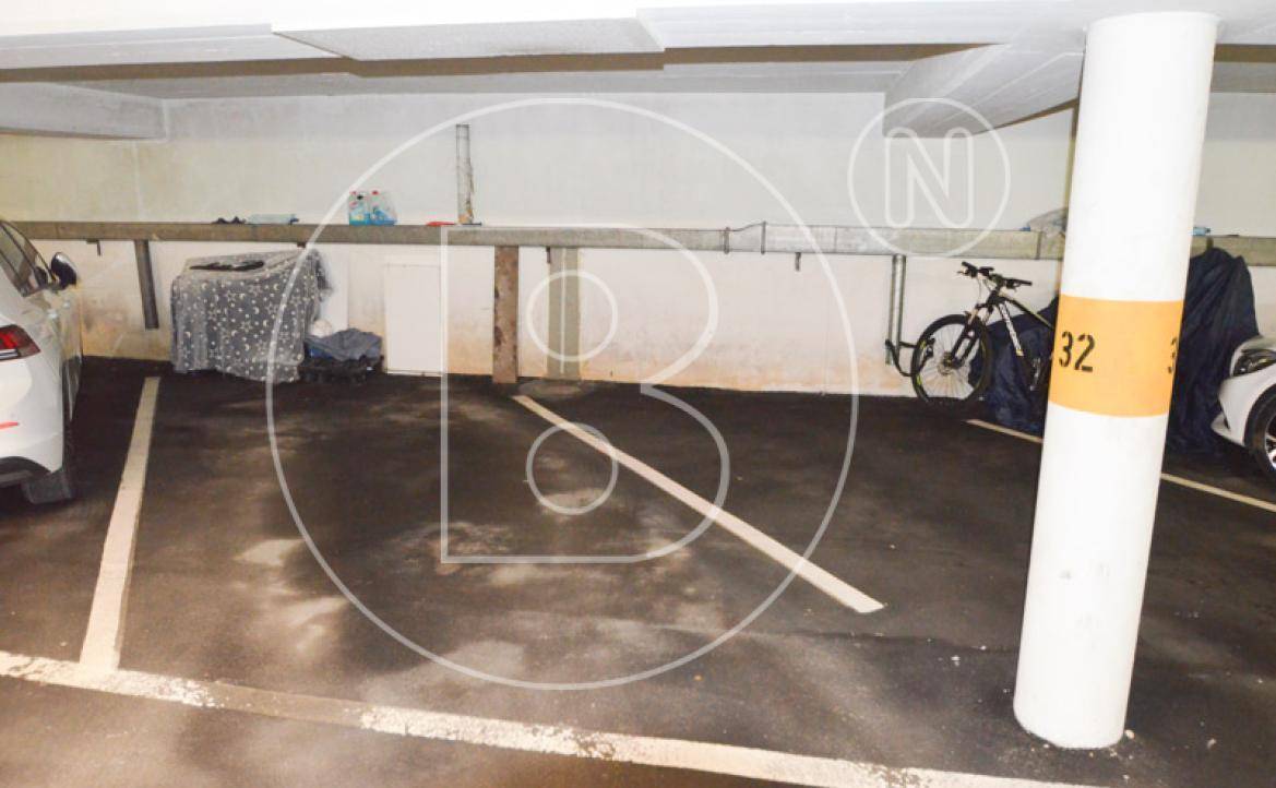 Einzelner Parkplatz in einer Tiefgarage mit Betonstütze und Abstellmöglichkeiten im Hintergrund.