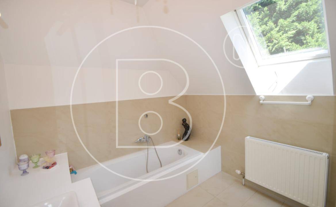 Badezimmer mit Badewanne unter einem Dachfenster und beigefarbenen Fliesen.