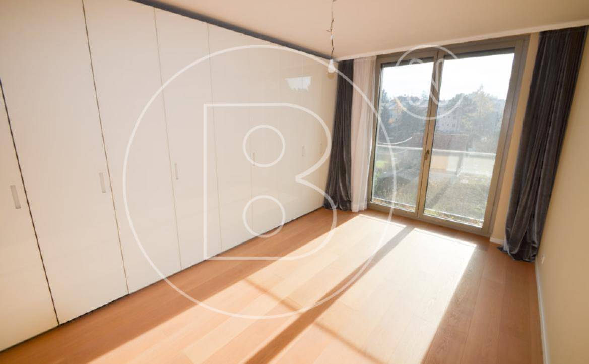 Helles Schlafzimmer mit Einbauschränken, Holzboden und Zugang zu einem Balkon oder einer Terrasse.