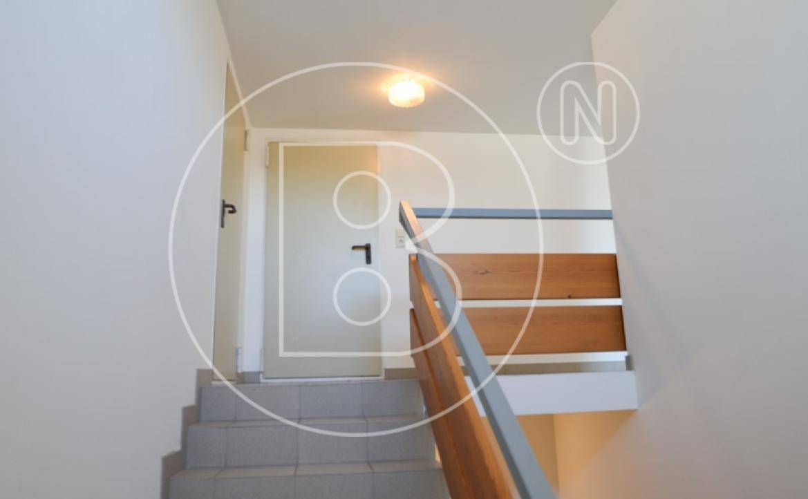 Heller Treppenaufgang mit Fliesenstufen und Holzgeländer in einem Mehrfamilienhaus.