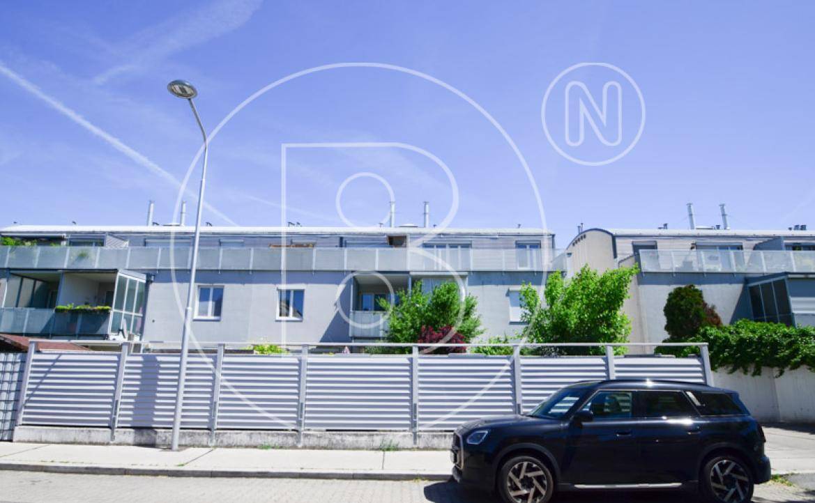 Fassade eines modernen Wohngebäudes mit Balkonen und einem schützenden Zaun im Vordergrund.