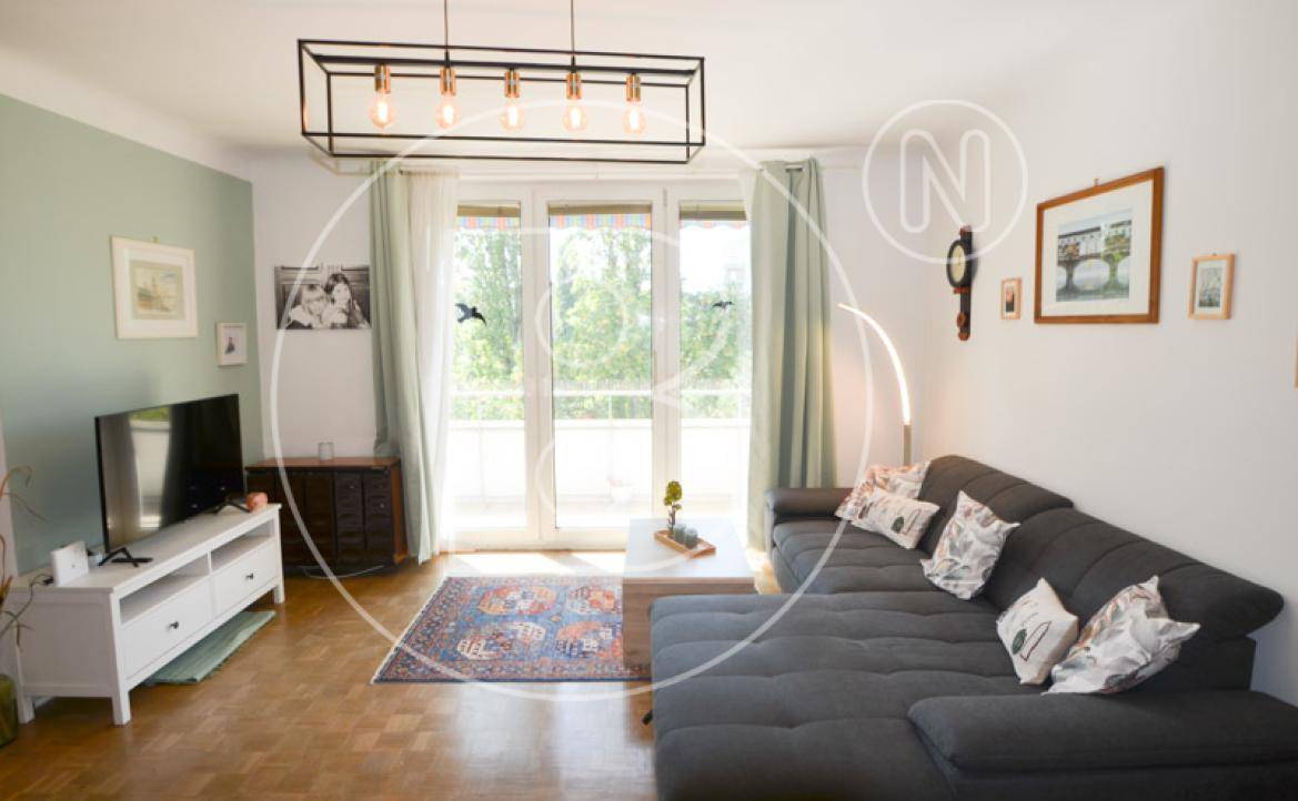 Gemütlicher Wohnbereich mit großem Sofa, Fernseher und hellen Fenstern, die viel Tageslicht hereinlassen.