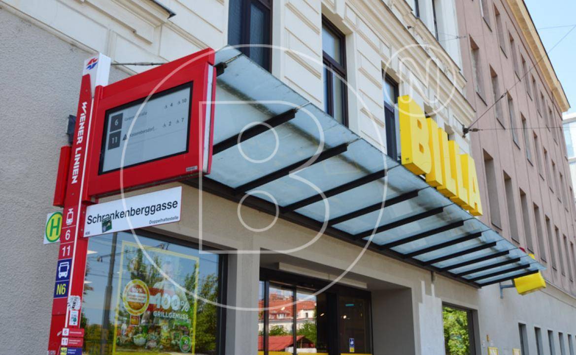 Geschäftsgebäude mit BILLA-Supermarkt und einer Bushaltestelle davor, geschützt durch ein Glasvordach.