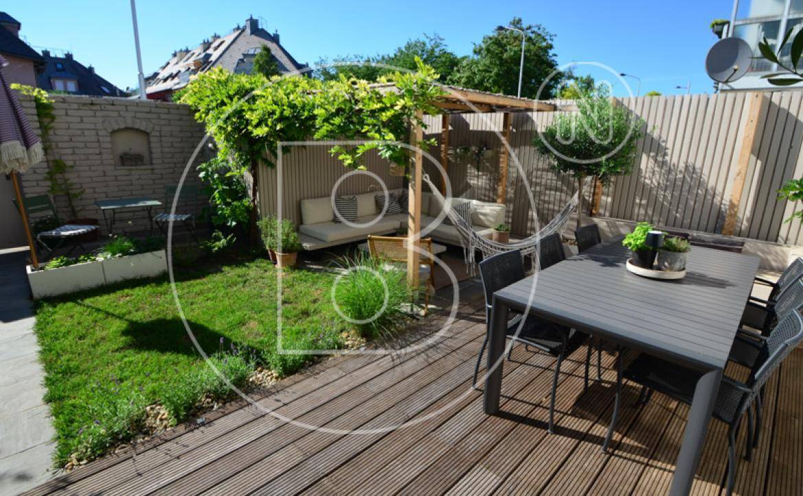 Geräumige Holzterrasse mit Essbereich, Lounge-Möbeln unter Pergola und kleinem Garten.