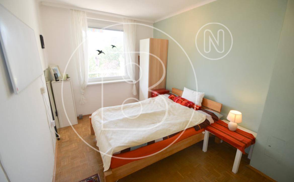 Helles Schlafzimmer mit Einzelbett, Holzfußboden und Fenster mit Blick ins Grüne.
