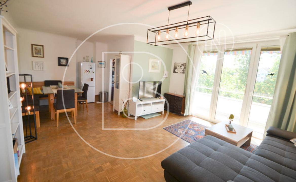 Heller offener Wohn- und Essbereich mit Parkettboden und großen Fenstern, die zum Balkon führen.