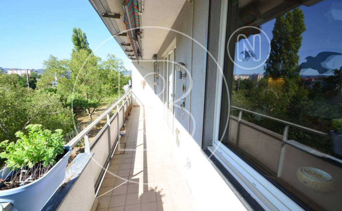 Langer Balkon mit Fliesenboden und Blick auf die grünen Bäume und die Umgebung an einem sonnigen Tag.