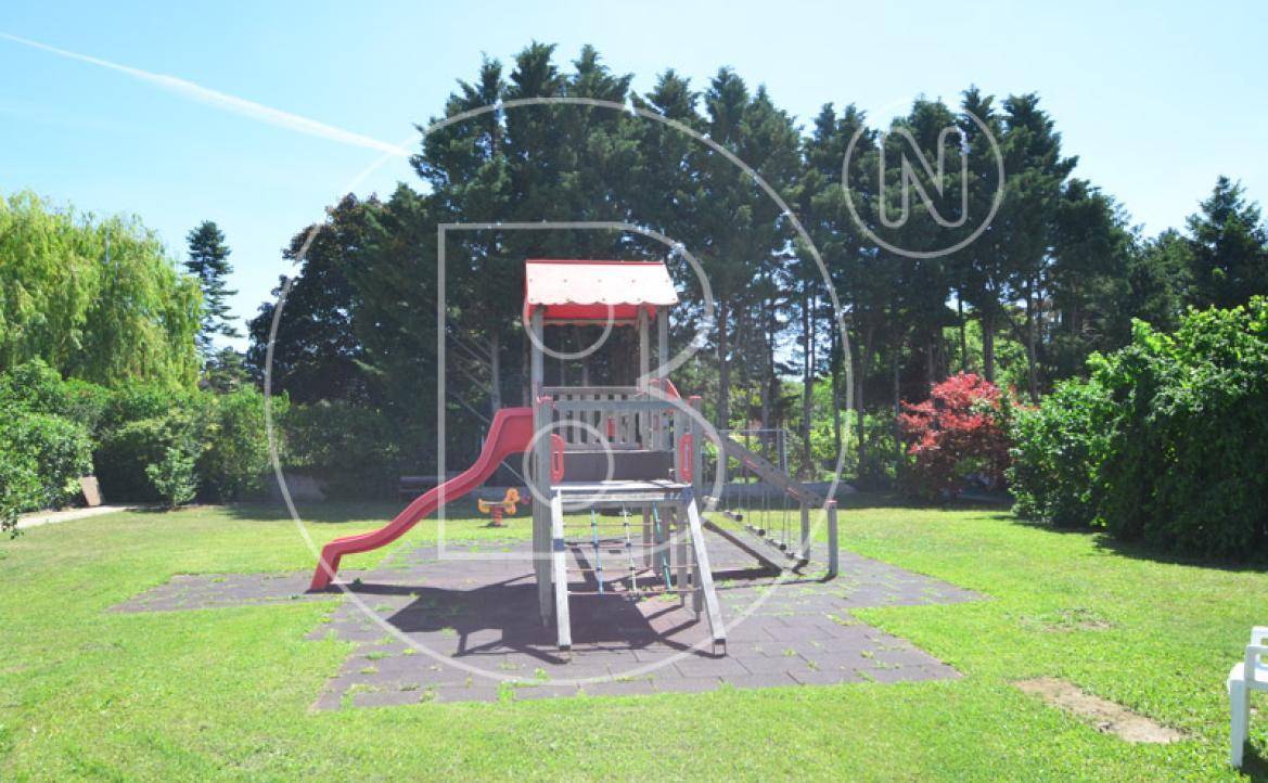 Kinderspielplatz mit Rutsche und Klettergerüst in einer weitläufigen grünen Gartenanlage.