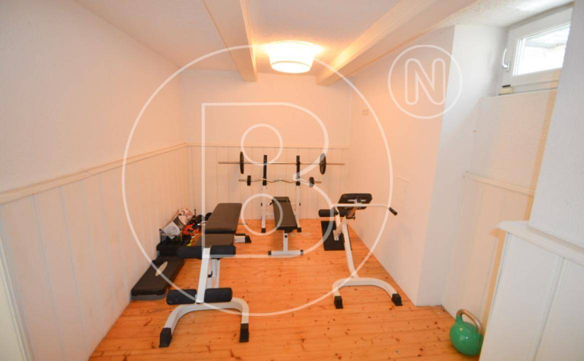Fitnessraum im Untergeschoss mit Trainingsgeräten und sichtbaren Deckenbalken.