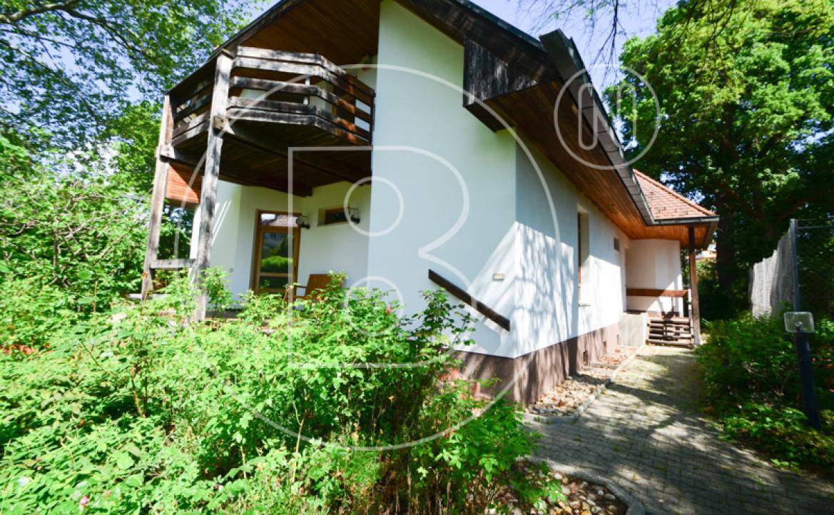 Seitenansicht des Hauses mit Holzbalkonen und üppiger Bepflanzung im Vordergrund.