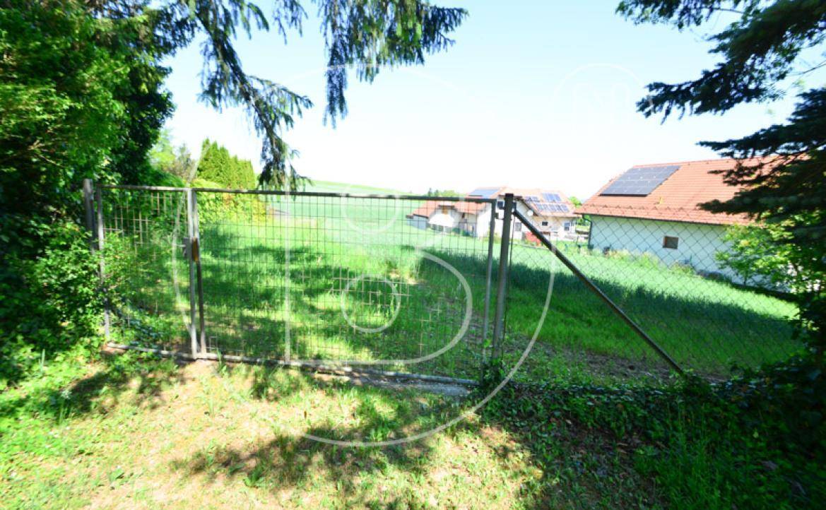 Blick über einen Zaun auf ein Feld mit Häusern und Solaranlagen in der Ferne.