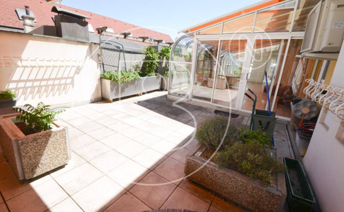 Sonniger Terrassenbereich mit Fliesenboden und bepflanzten Blumenkästen.