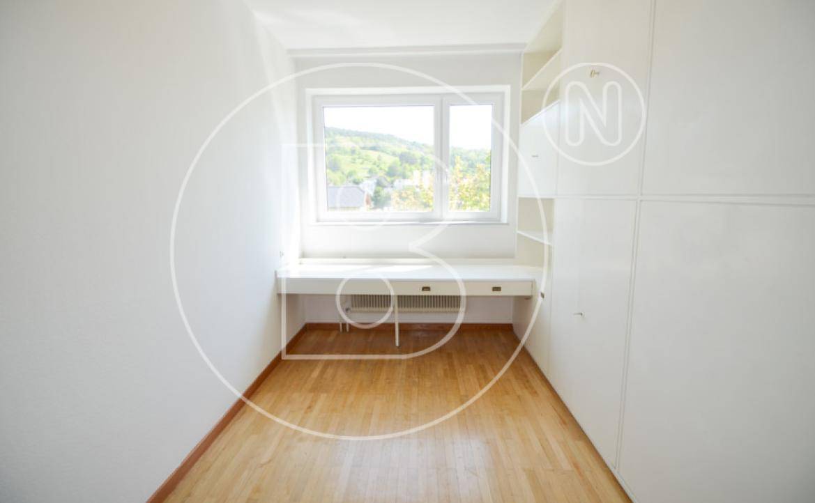 Helles Schlafzimmer mit Holzboden, Einbauschreibtisch unter dem Fenster und Blick ins Grüne.