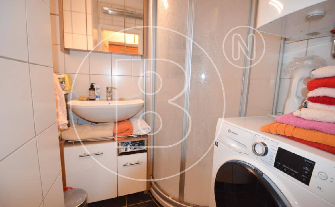 Badezimmer mit Dusche, Waschbecken und Waschmaschine, funktional und hell gefliest.