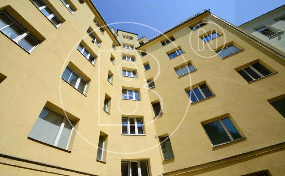 Blick nach oben auf die gelbe Fassade eines Mehrfamilienhauses im Innenhof mit vielen Fenstern.