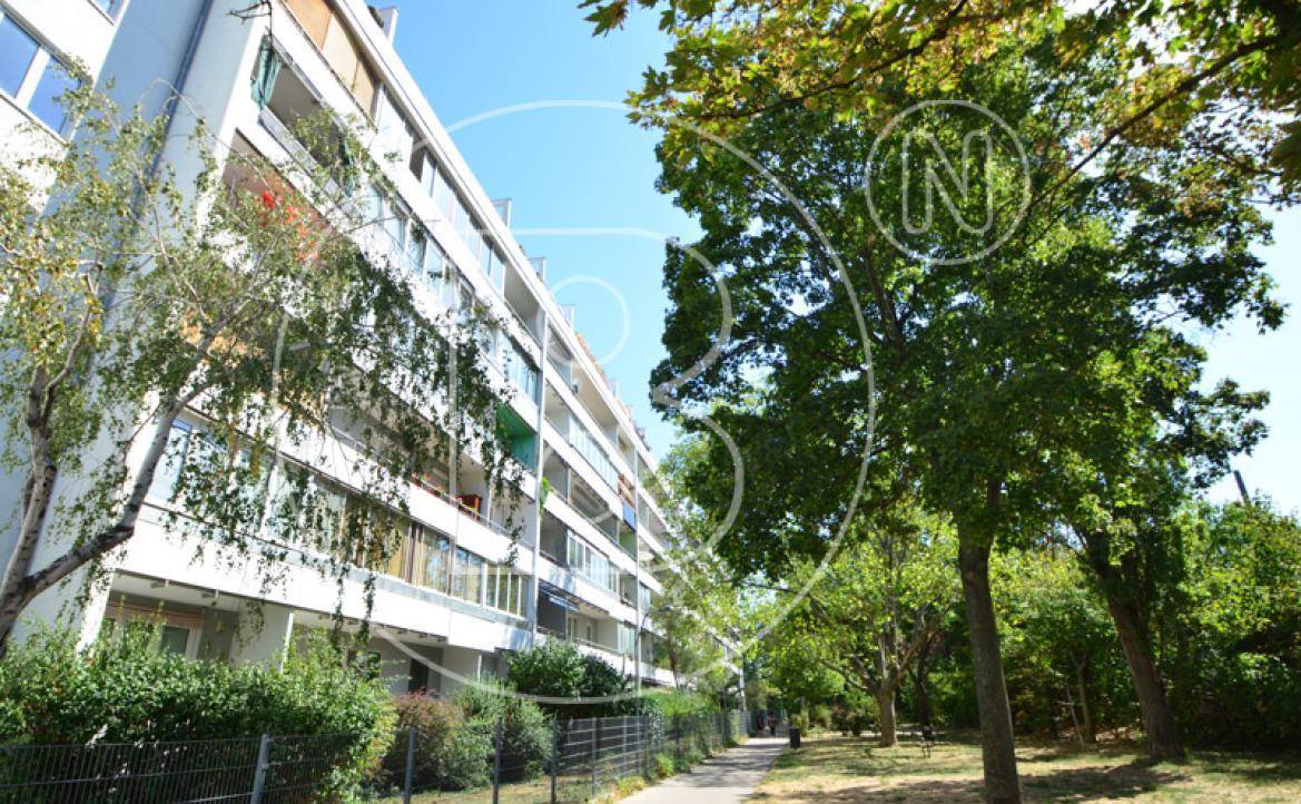 Seitenansicht eines Apartmentgebäudes umgeben von üppigen Bäumen und einer gepflegten Grünfläche.