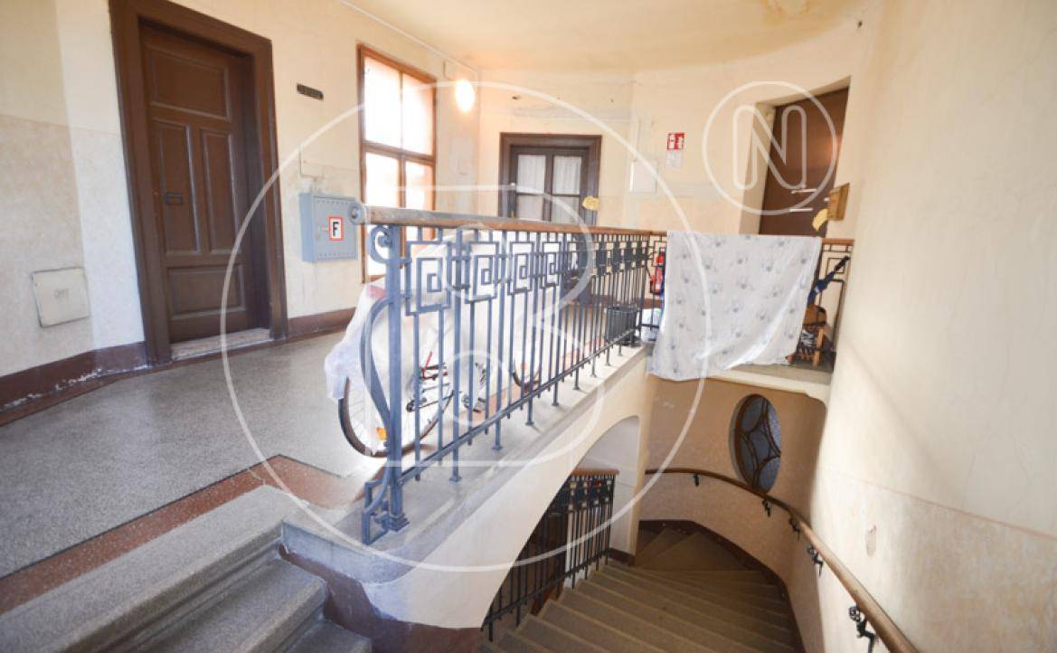 Geräumiges Treppenhaus mit kunstvollem Geländer, Holztüren und Terrazzoboden auf dem Podest, typisch für einen Altbau.
