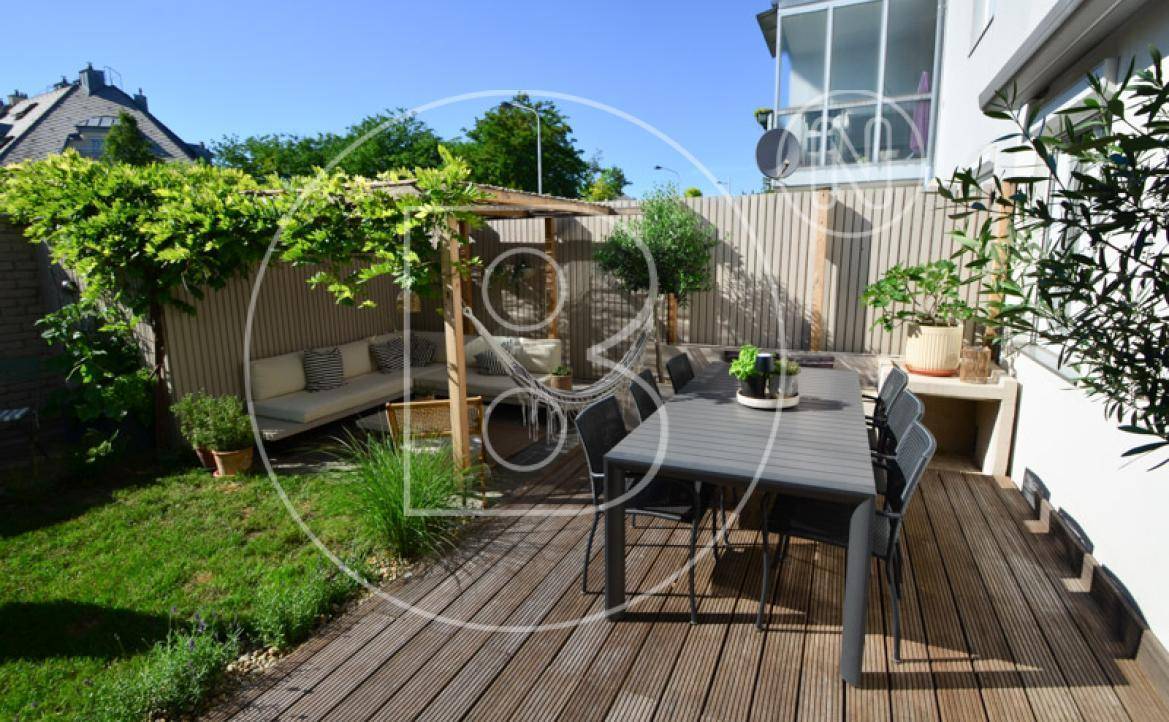 Weitläufige Holzterrasse mit Essbereich, Lounge-Möbeln unter Pergola und gepflegtem Garten.