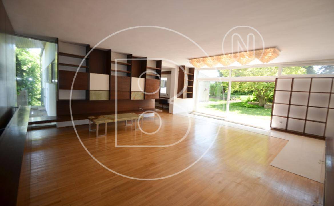 Geräumiges Wohnzimmer mit großen Fenstern, Holzboden und integrierten Regalsystemen.