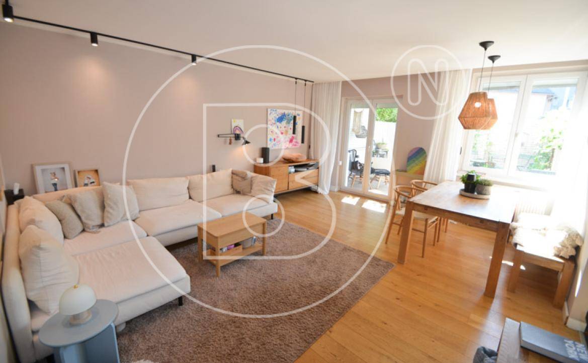 Heller Wohn-Essbereich mit Holzboden, großem Sofa und Zugang zur Terrasse.
