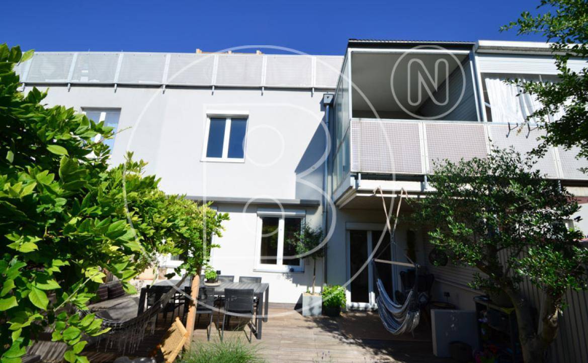 Rückseite des Hauses mit großer Holzterrasse, Garten und Balkon im Obergeschoss.