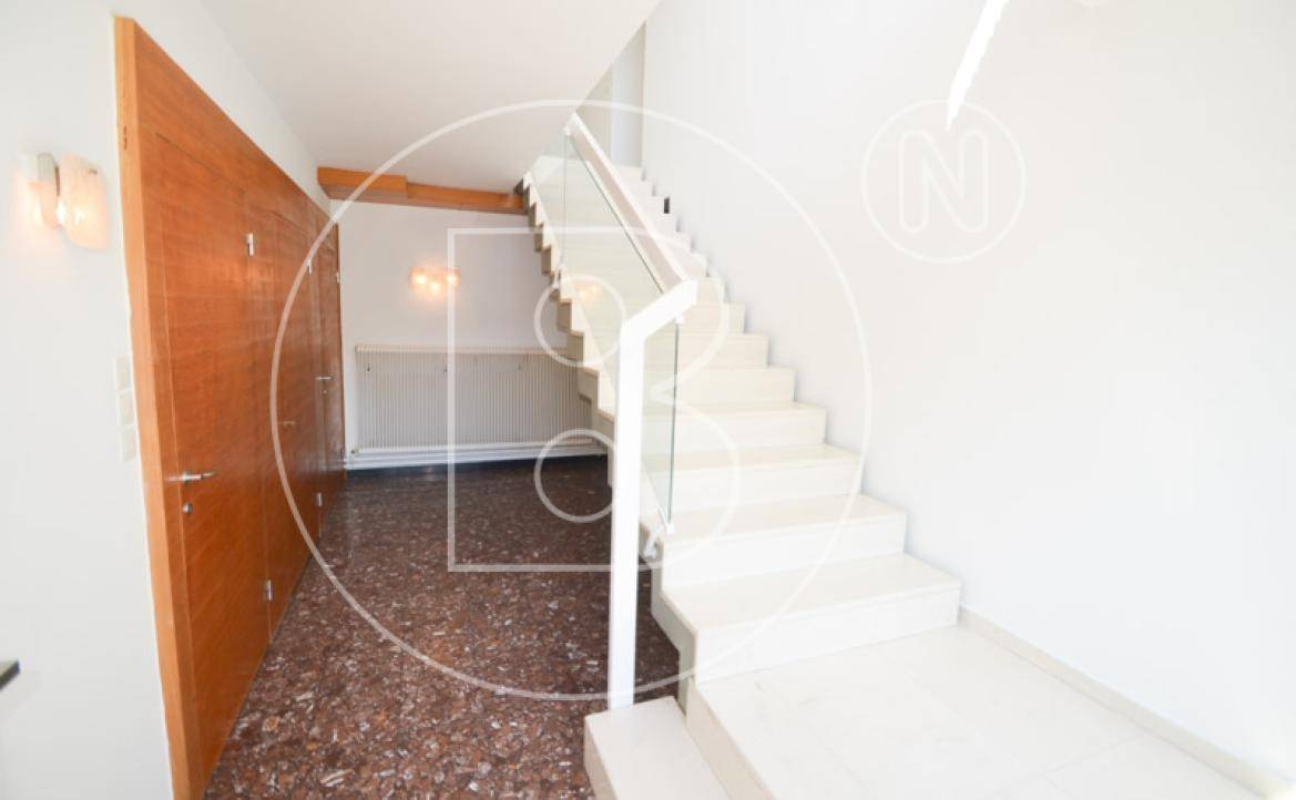 Heller Flur mit moderner Treppe und Terrazzoboden, der zu den oberen Etagen führt.
