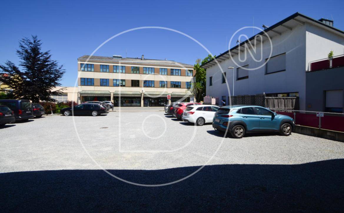 Weitläufiger Parkplatz mit Kiesbelag und dem Hauptgebäude im Hintergrund an einem sonnigen Tag.