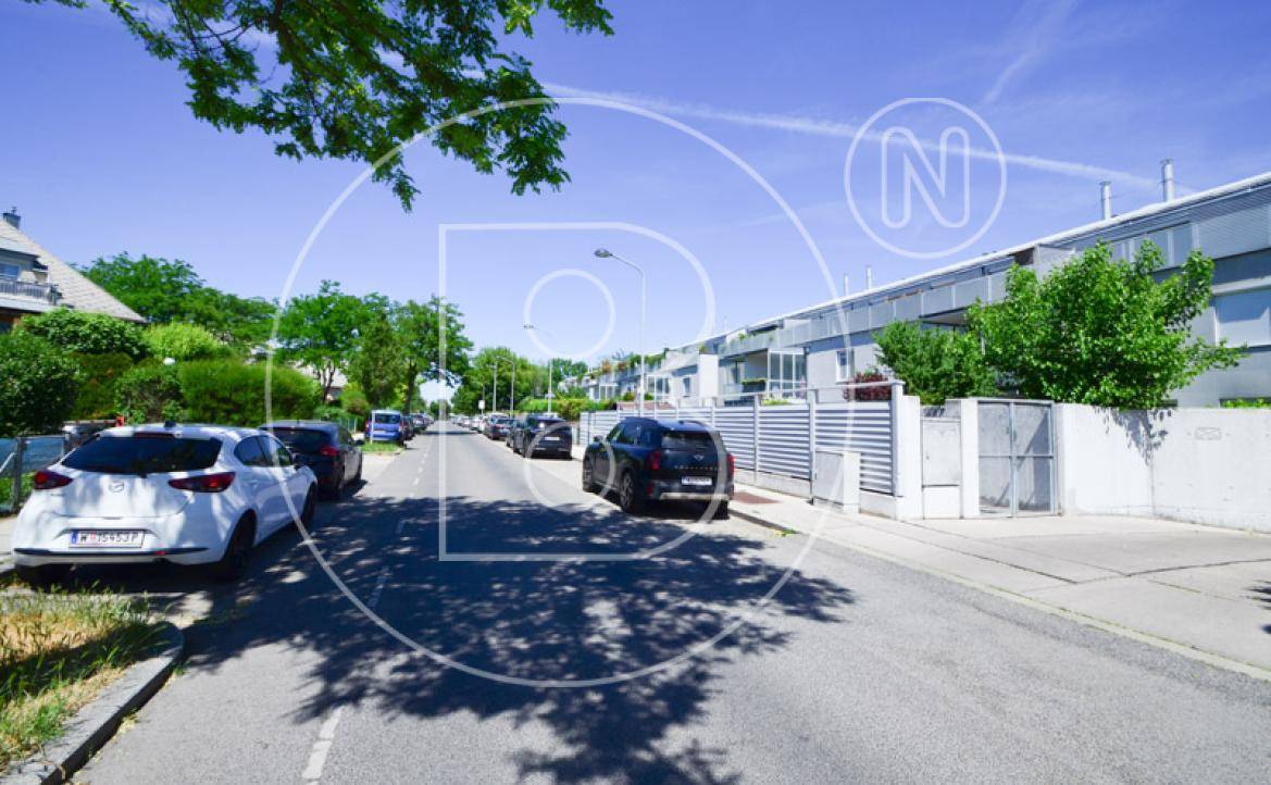 Ruhige Wohnstraße mit geparkten Fahrzeugen und modernen Reihenhäusern im Hintergrund.