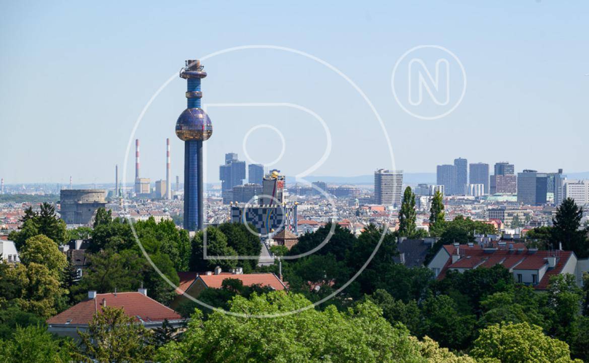 Panoramablick auf die Wiener Skyline mit markantem blauen Turm und grünen Bäumen.