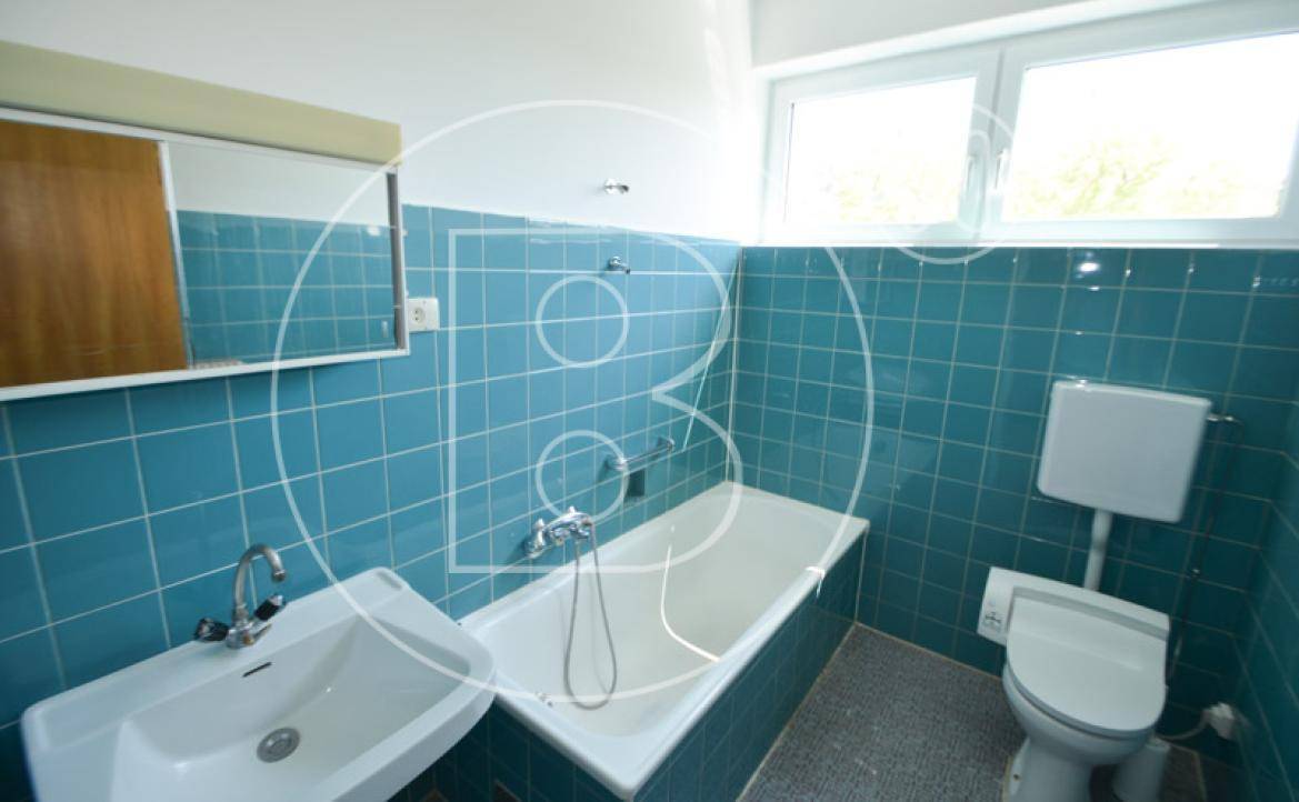 Badezimmer mit blauen Fliesen, Badewanne, Waschbecken und Toilette, sowie einem Fenster für Tageslicht.