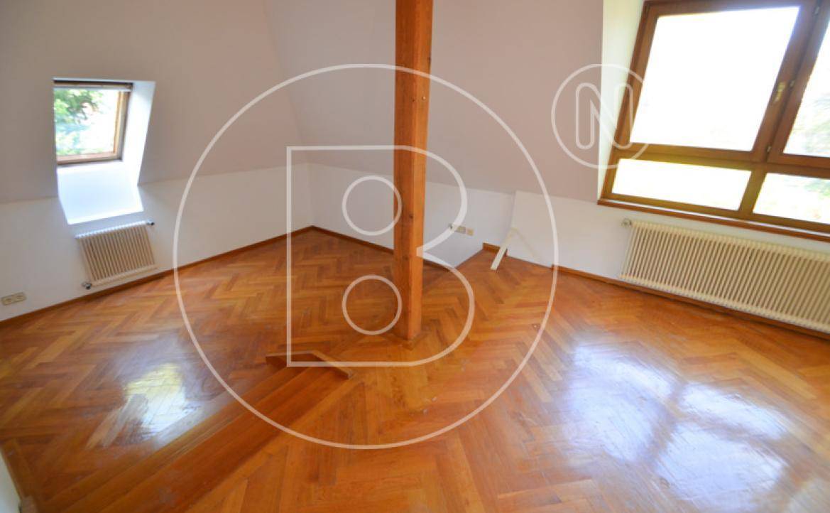 Geräumiges Zimmer im Dachgeschoss mit Holzbalken, viel Tageslicht und schrägen Wänden.