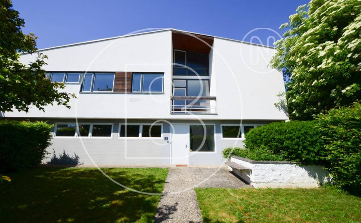 Moderne Hausfassade mit großen Fenstern und einem gepflegten Vorgarten unter strahlendem Himmel.