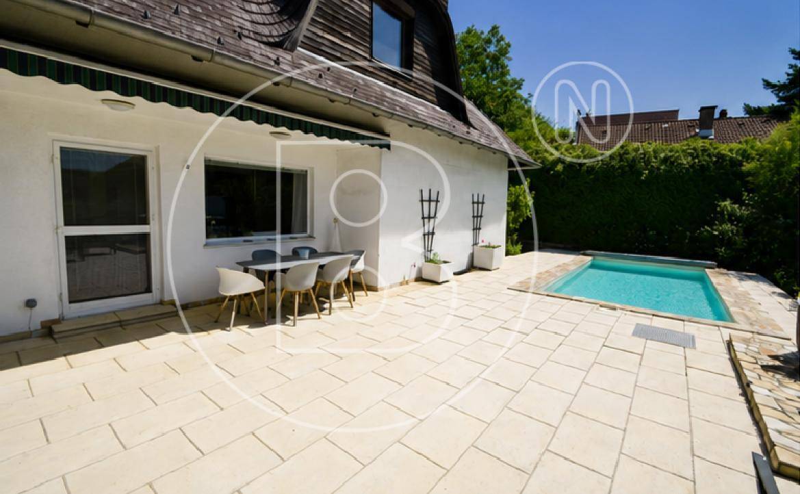 Hausfassade mit überdachtem Essbereich auf der Terrasse und angrenzendem Swimmingpool.
