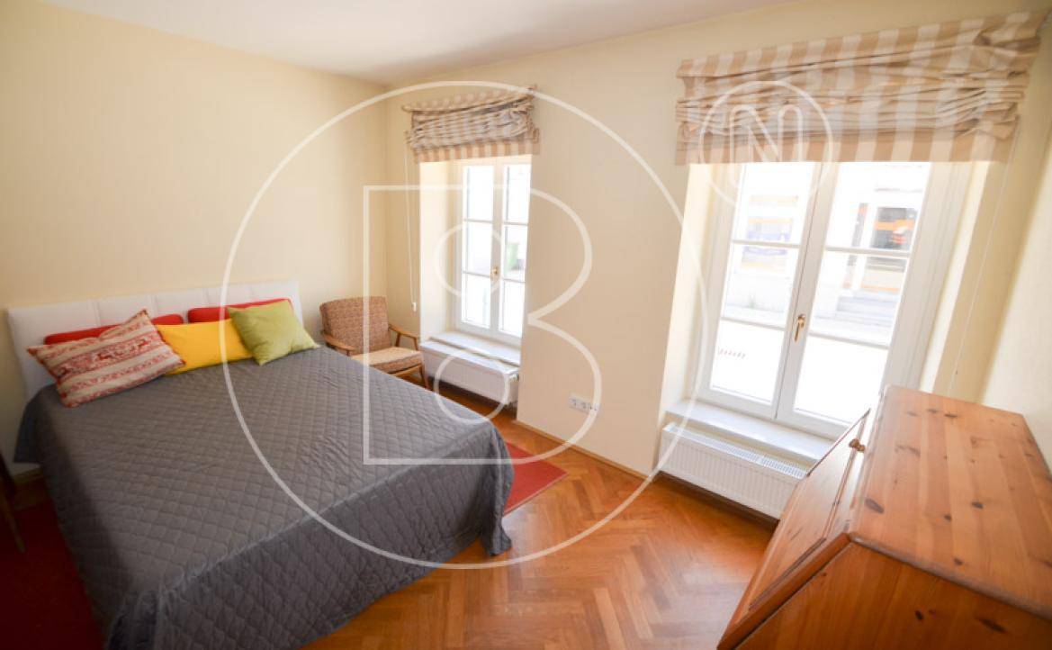 Gemütliches Schlafzimmer mit Doppelbett, Holzmöbeln und zwei hohen Fenstern.