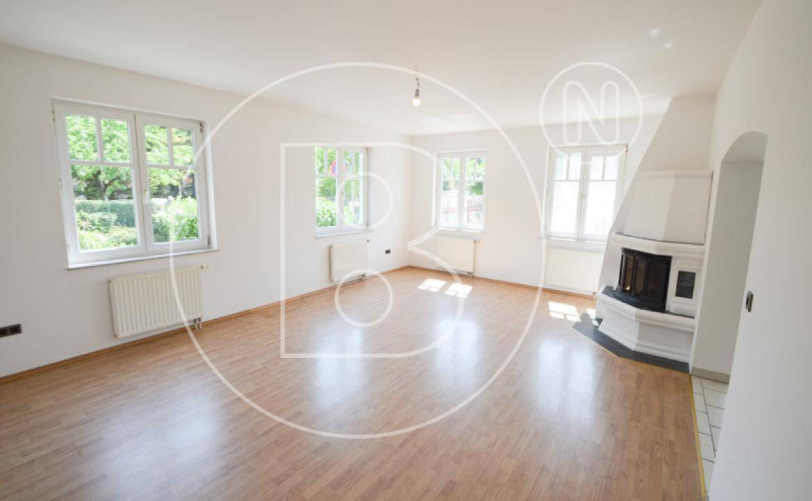 Geräumiges Wohnzimmer mit Parkettboden, Kamin und mehreren Fenstern für viel Tageslicht.