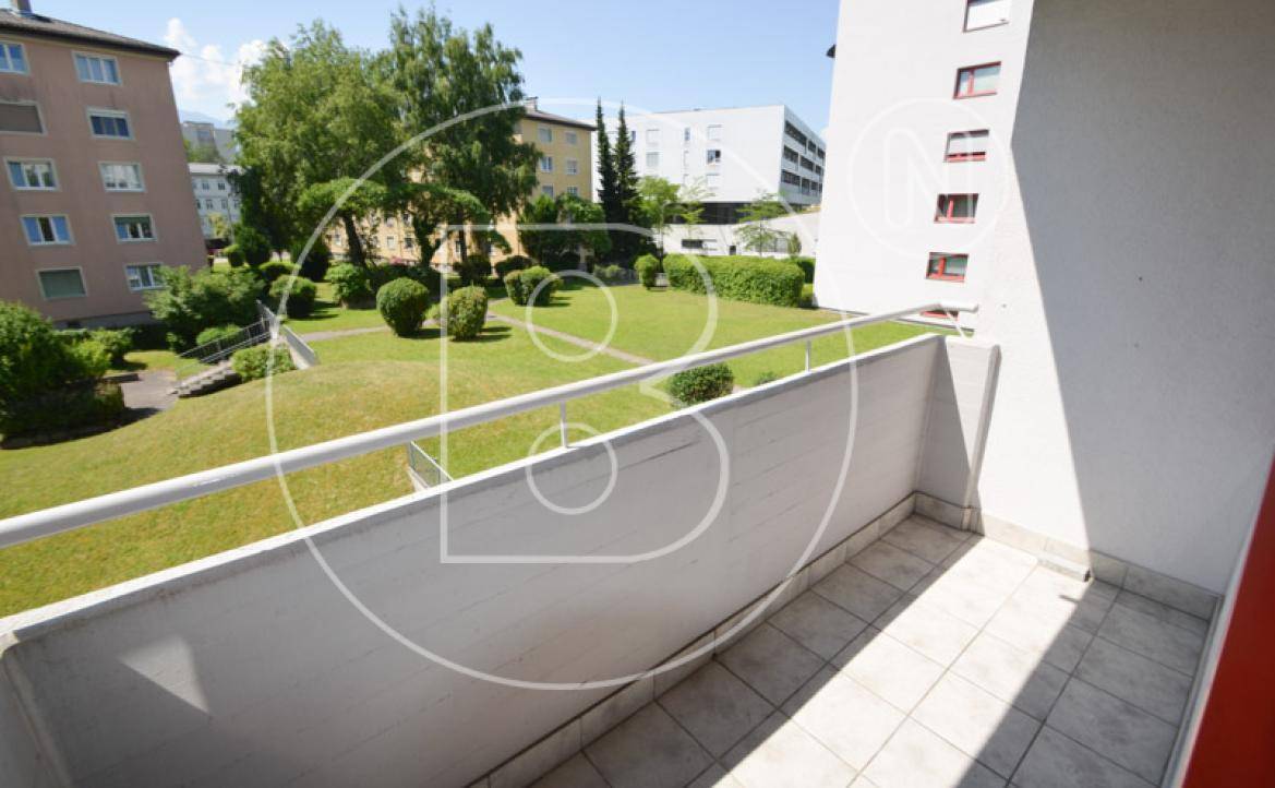 Balkon mit Blick auf eine weitläufige grüne Gartenanlage und umliegende Wohngebäude.