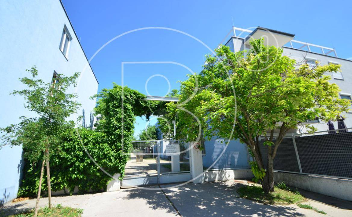 Eingangsbereich eines modernen Wohnkomplexes mit üppiger Begrünung und einem sicheren Tor.