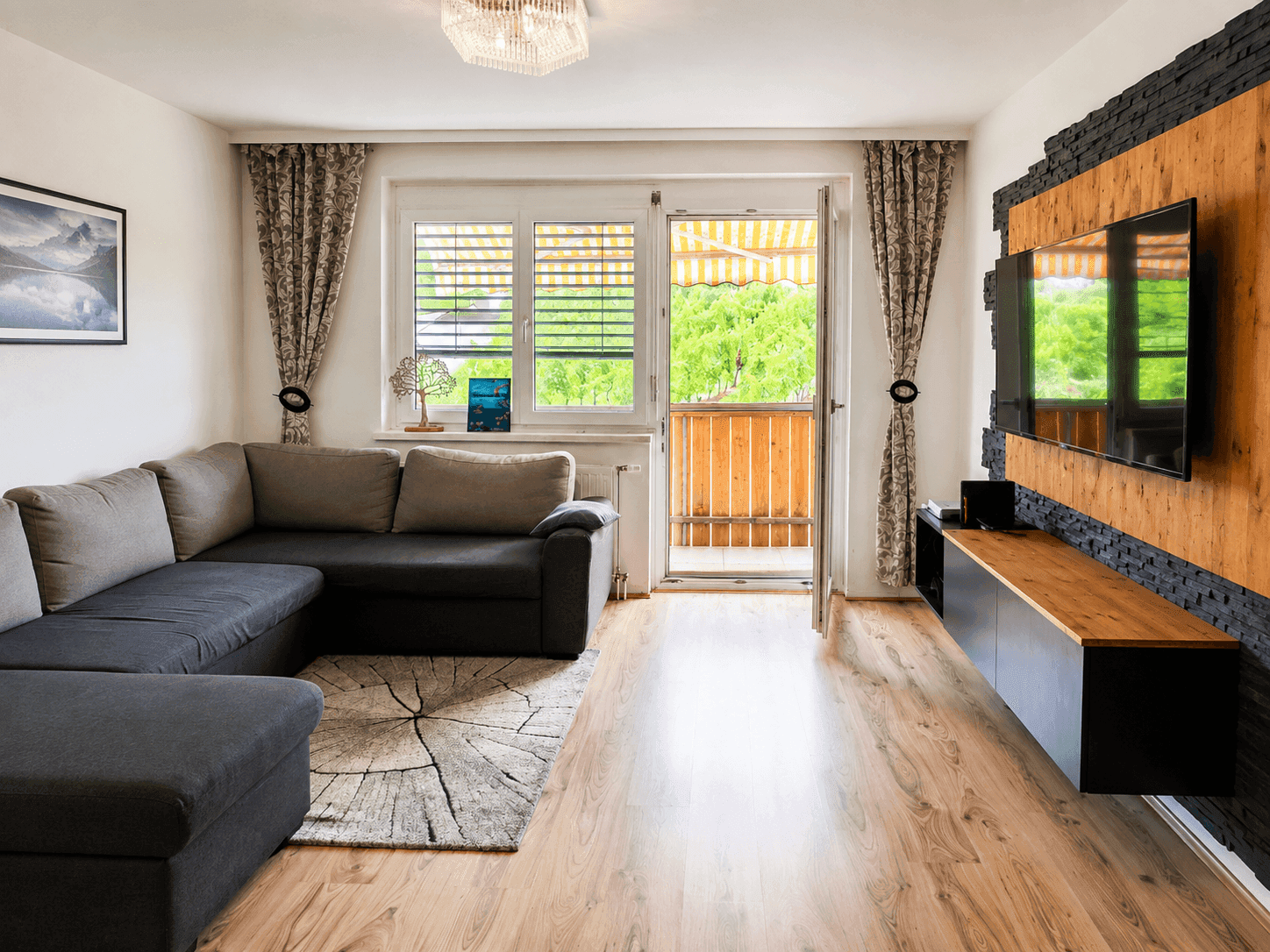Gemütliches Wohnzimmer mit Holzboden, Ecksofa und Zugang zu einem kleinen Balkon.