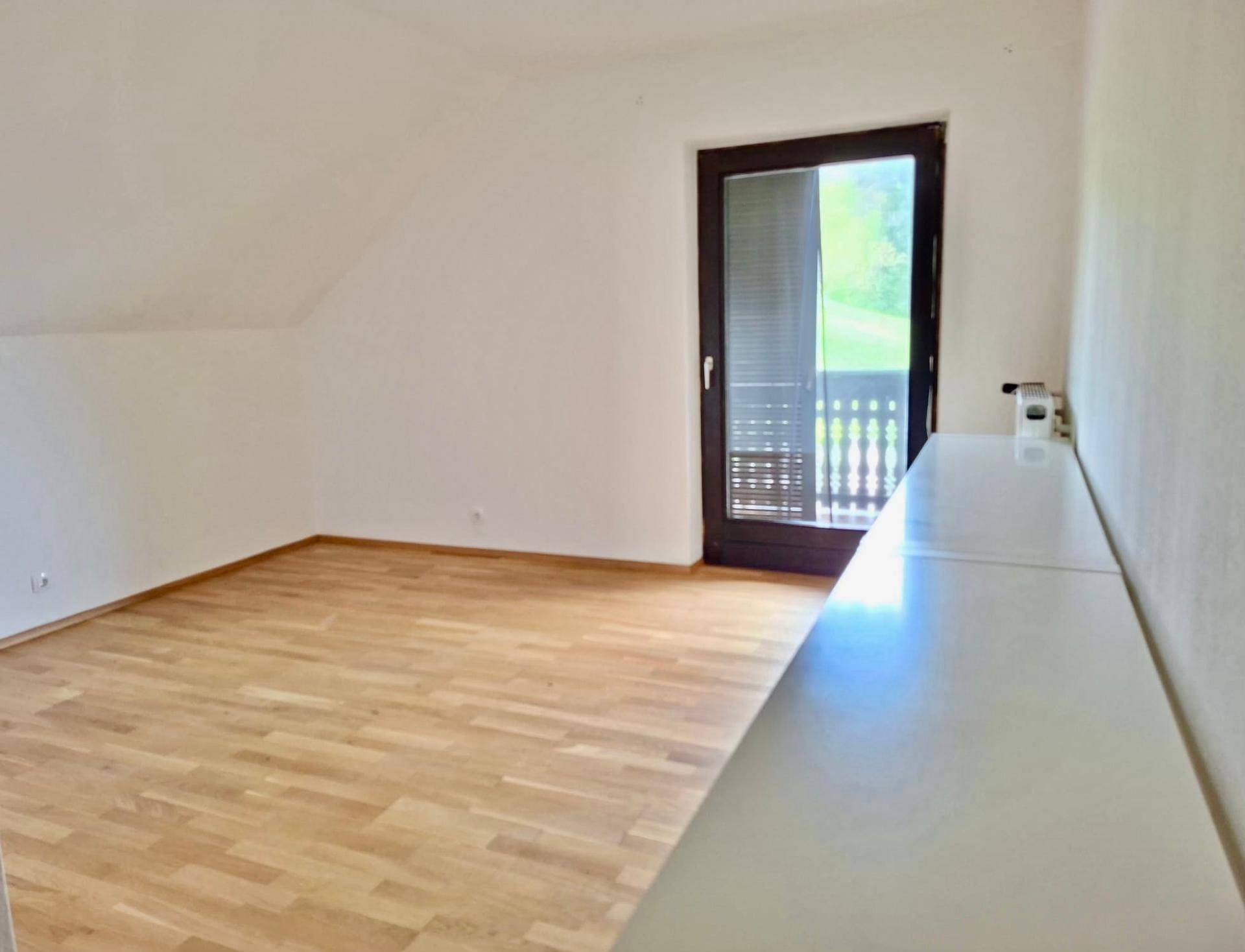 Helles Zimmer mit Holzfußboden und Zugang zu einem kleinen Balkon mit Blick ins Freie.