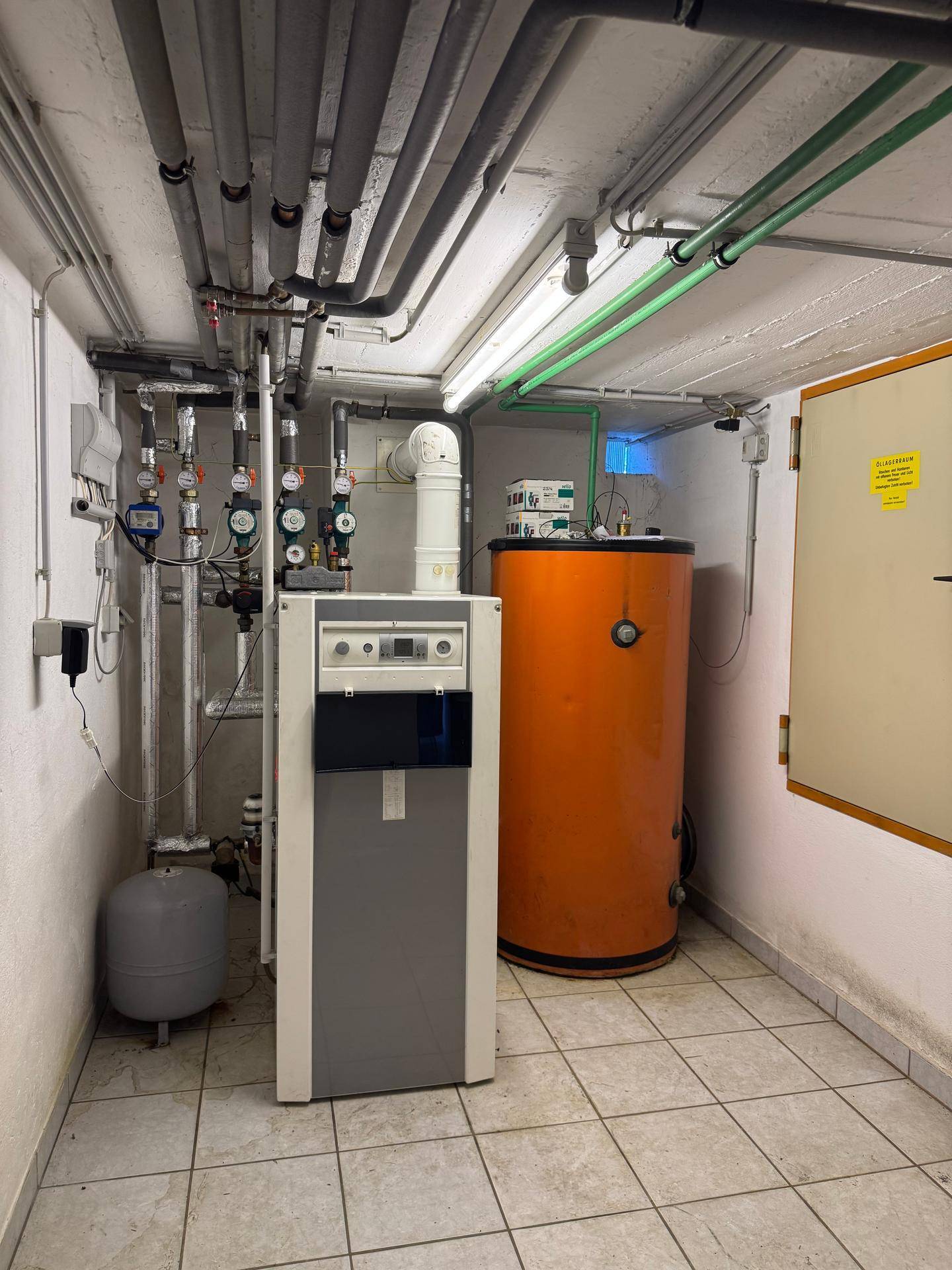 Heizungsraum mit Kessel und Warmwasserspeicher, sowie zahlreichen Rohrleitungen.