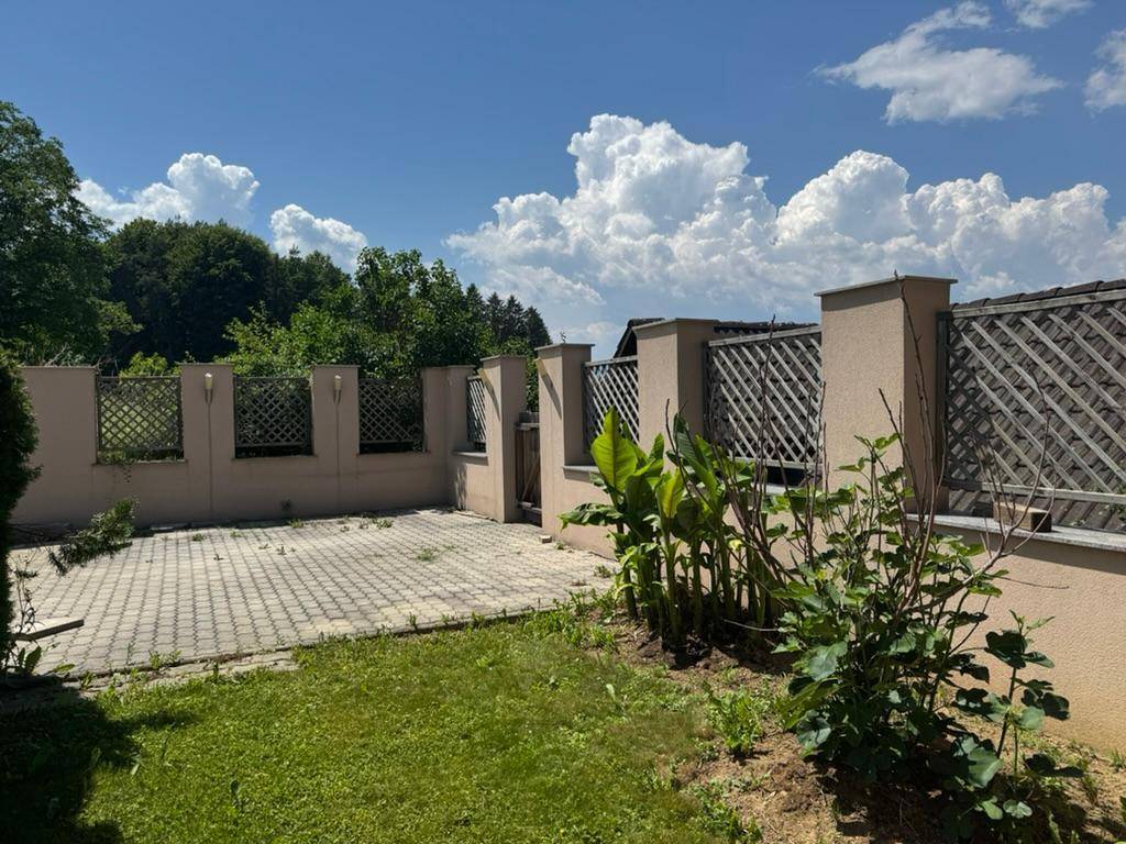 Gepflasterter Terrassenbereich mit Rasenfläche und dekorativem Zaun mit Rankgittern.