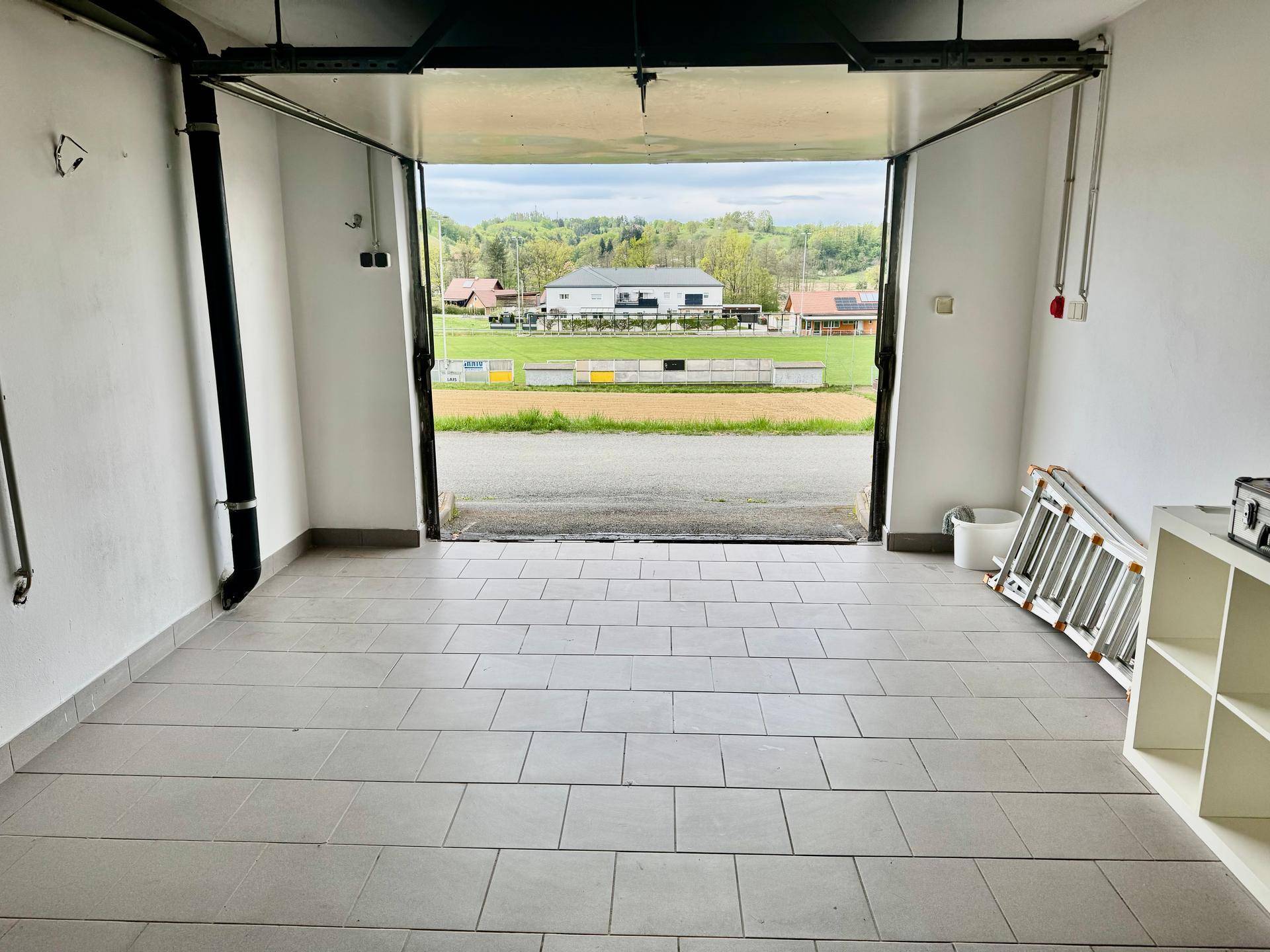 Geräumige Garage mit gefliestem Boden und Blick auf die ländliche Umgebung.