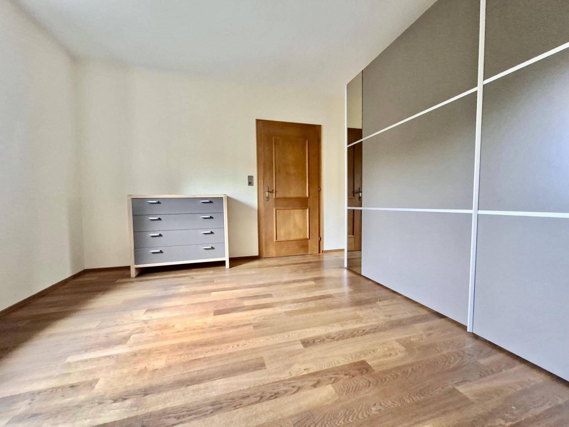 Schlafzimmer mit Holzfußboden, einem Kleiderschrank und einer Kommode in neutralen Farben.