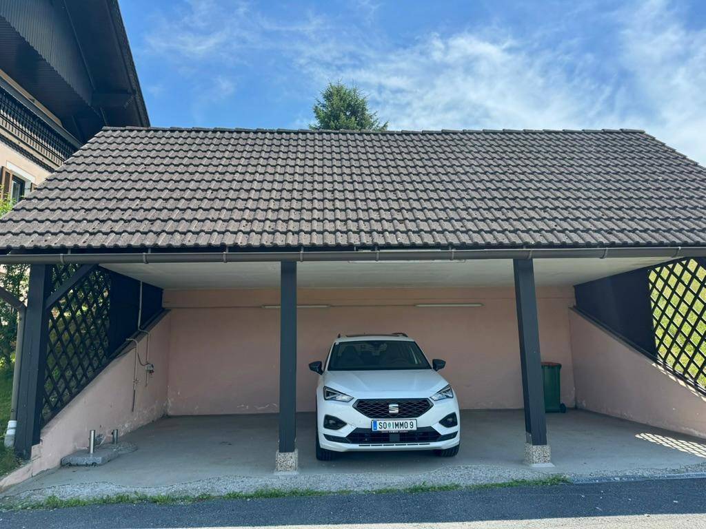 Nahaufnahme des Carports mit einem geparkten weißen Auto und einem Ziegeldach.
