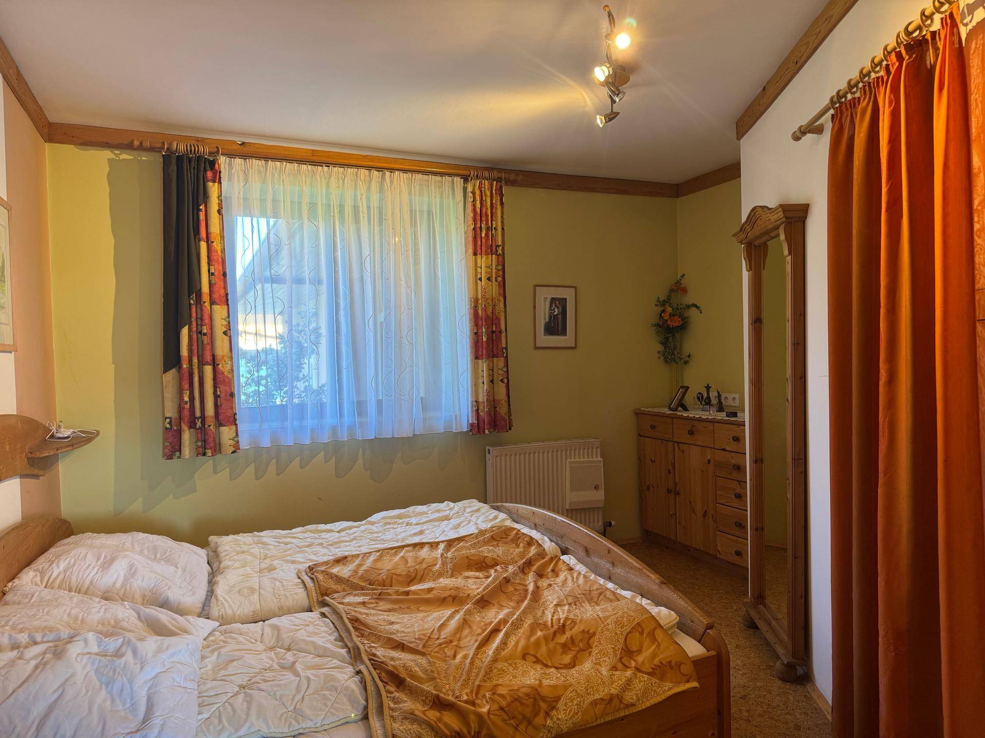 Schlafzimmer mit Holzbett, rustikalen Möbeln und einem Fenster mit Vorhängen.