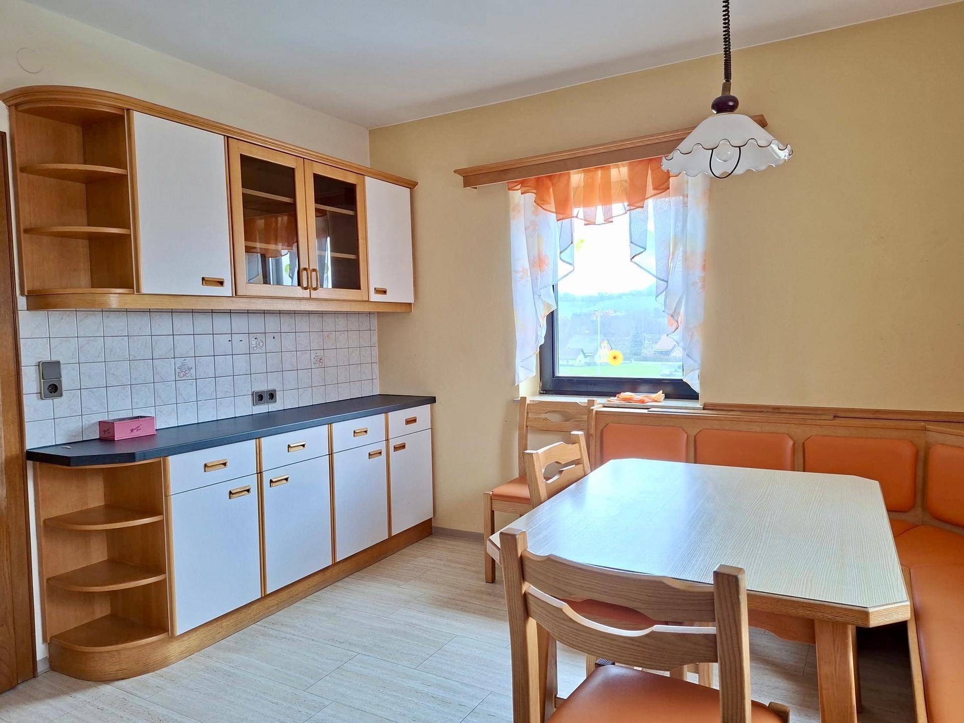 Gemütliche Wohnküche mit Holzelementen, Essbereich und Blick ins Grüne durch das Fenster.