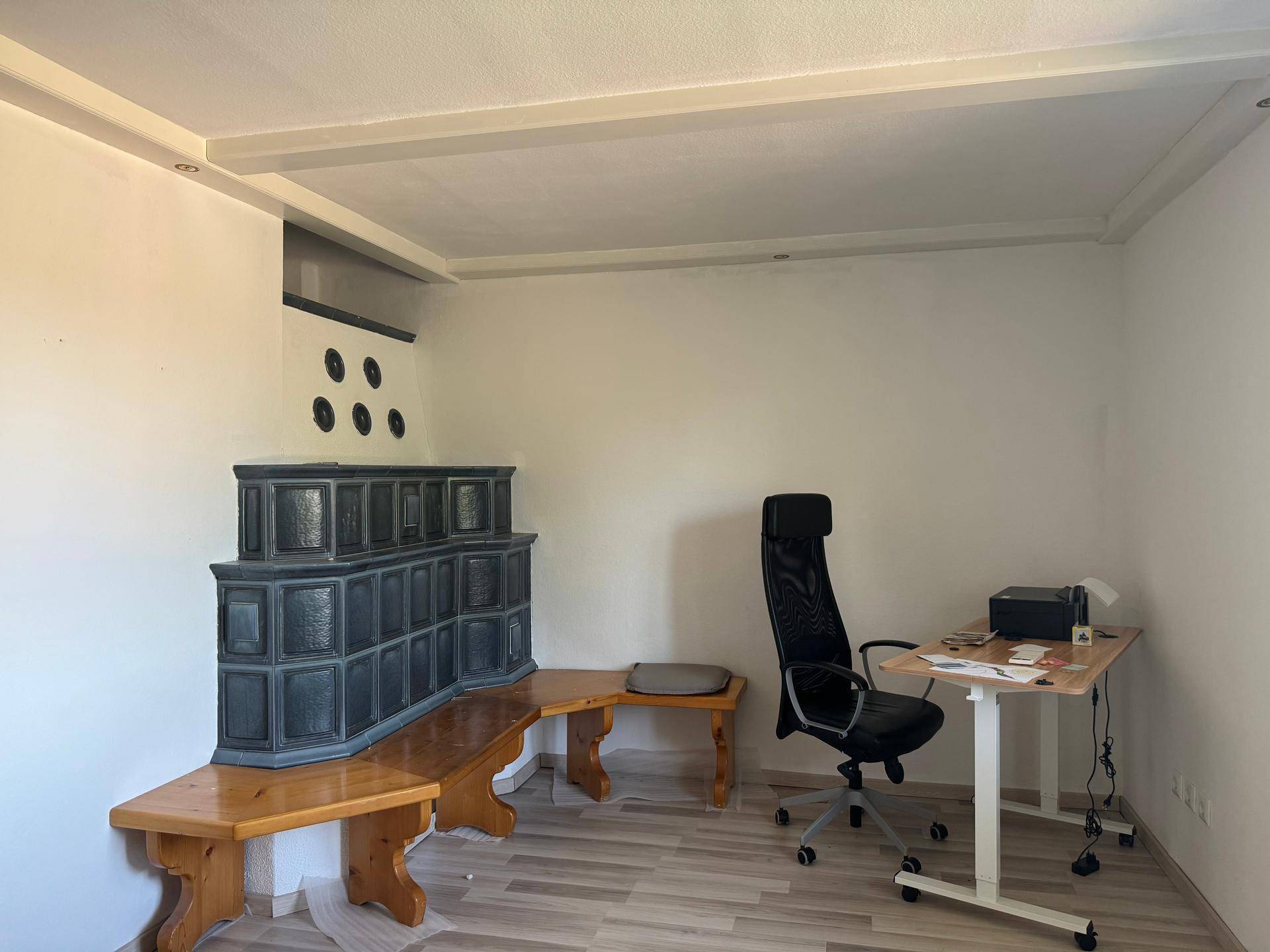 Arbeitszimmer mit traditionellem Kachelofen, Holzbänken und modernem Schreibtisch.
