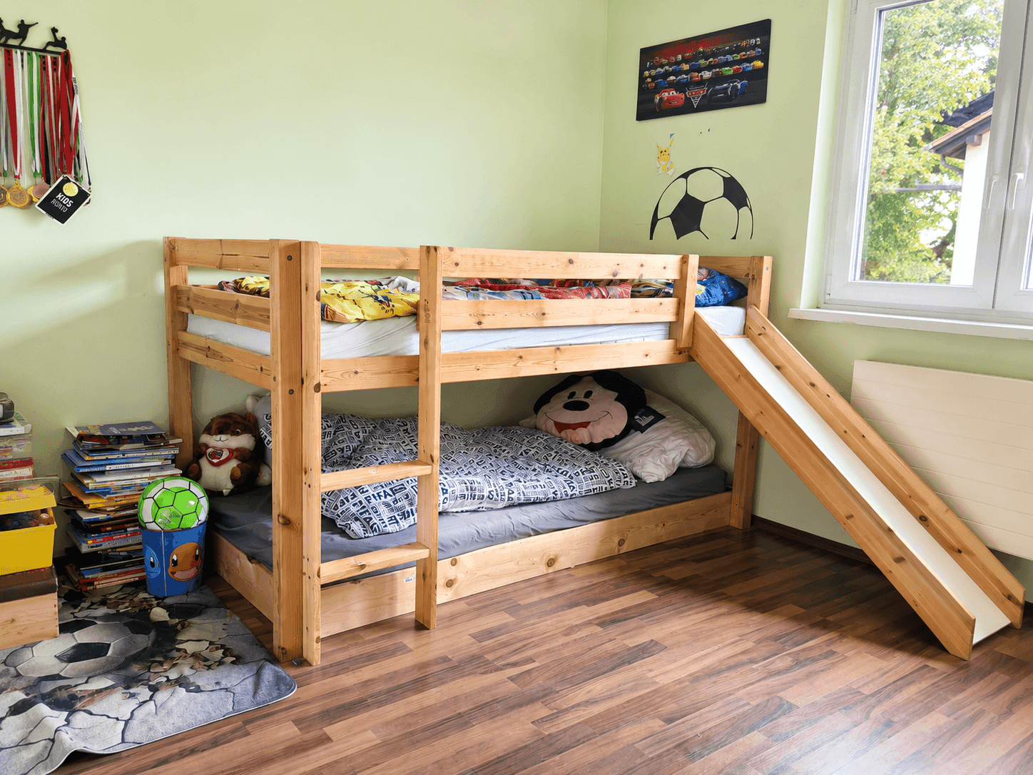 Kinderzimmer mit Etagenbett aus Holz, Spielzeug und Blick ins Grüne durch das Fenster.