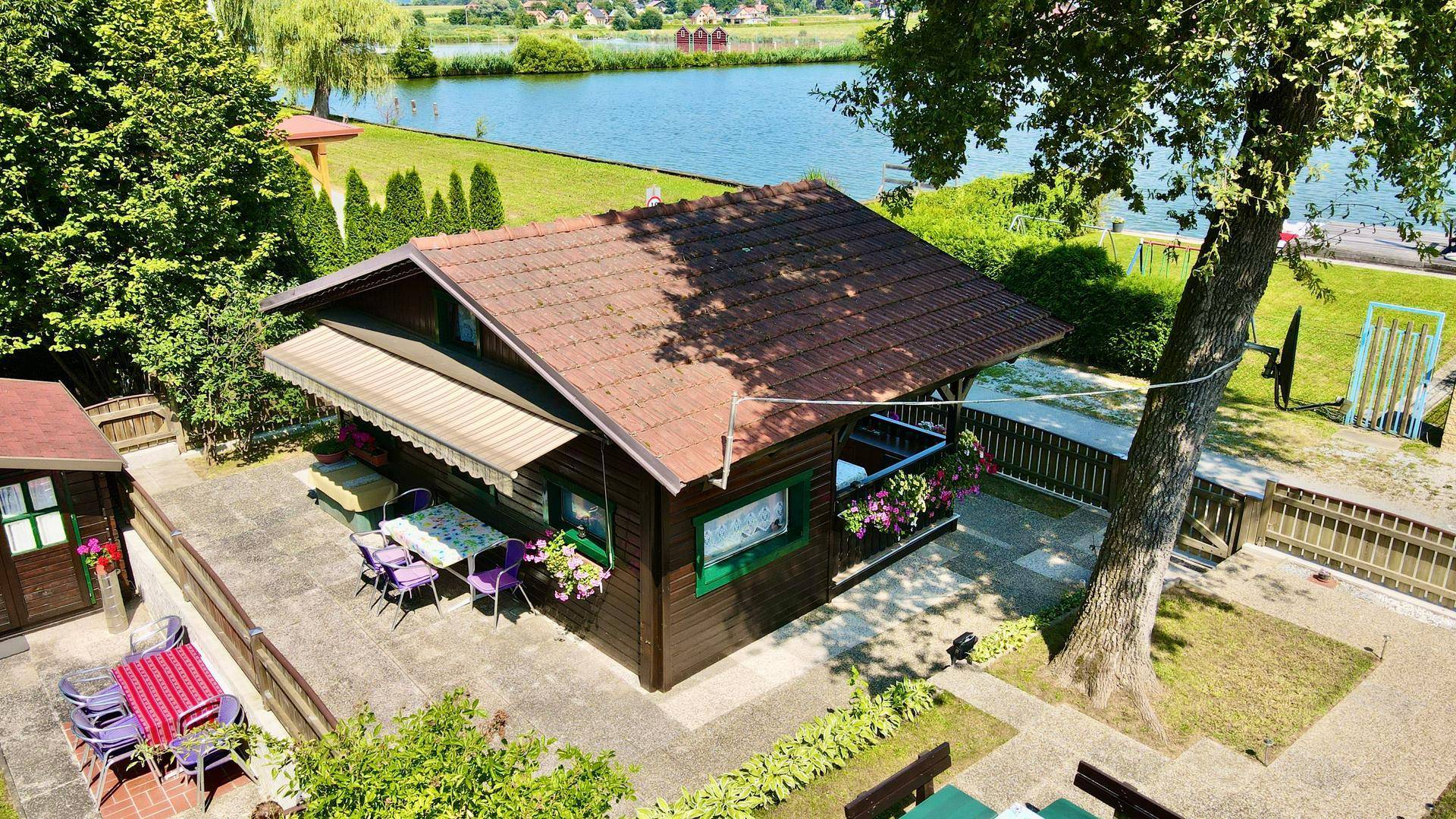 Ansicht des Holzhauses mit Terrasse, Nebengebäude und weitem Blick auf den See.
