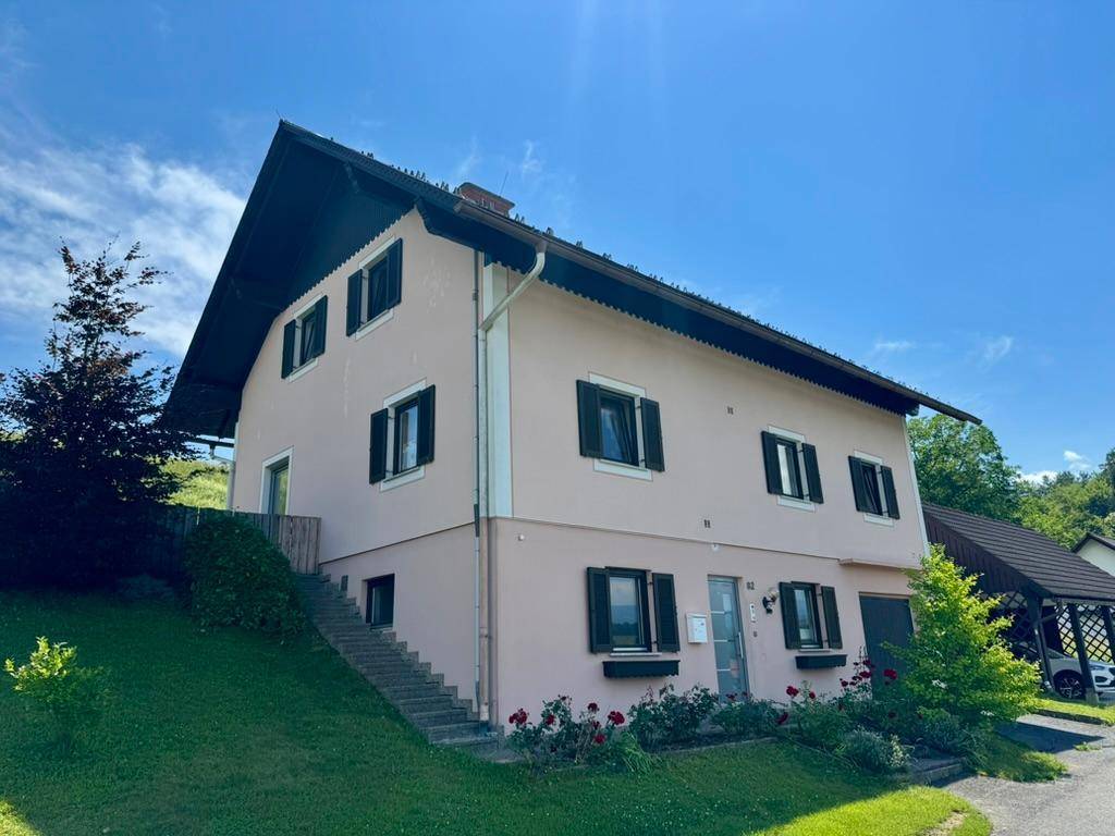 Weitläufige Ansicht des Hauses mit hellrosa Fassade, integrierter Garage und dem angrenzenden Carport.